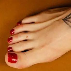 Nahaufnahme von Lady Samanthas Fuss mit rotem Nagellack und ihrem eleganten Fuss-Tattoo - Fussfetisch Zürich